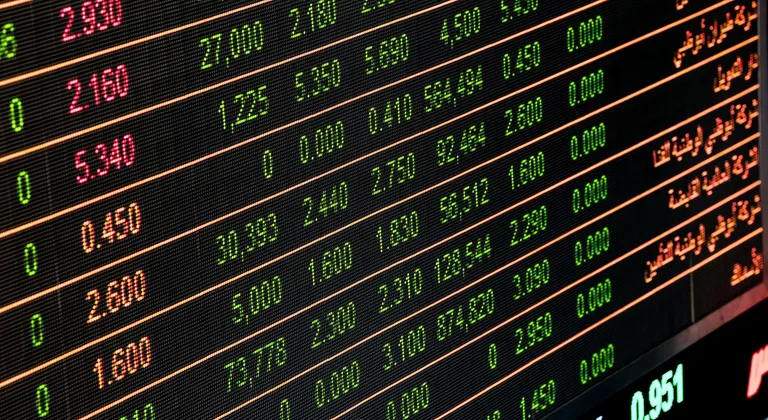 شاشة تداول إلكترونية في قاعة بورصة تعرض مؤشرات الأسهم وأرقاماً مالية متغيرة باللونين الأحمر والأخضر